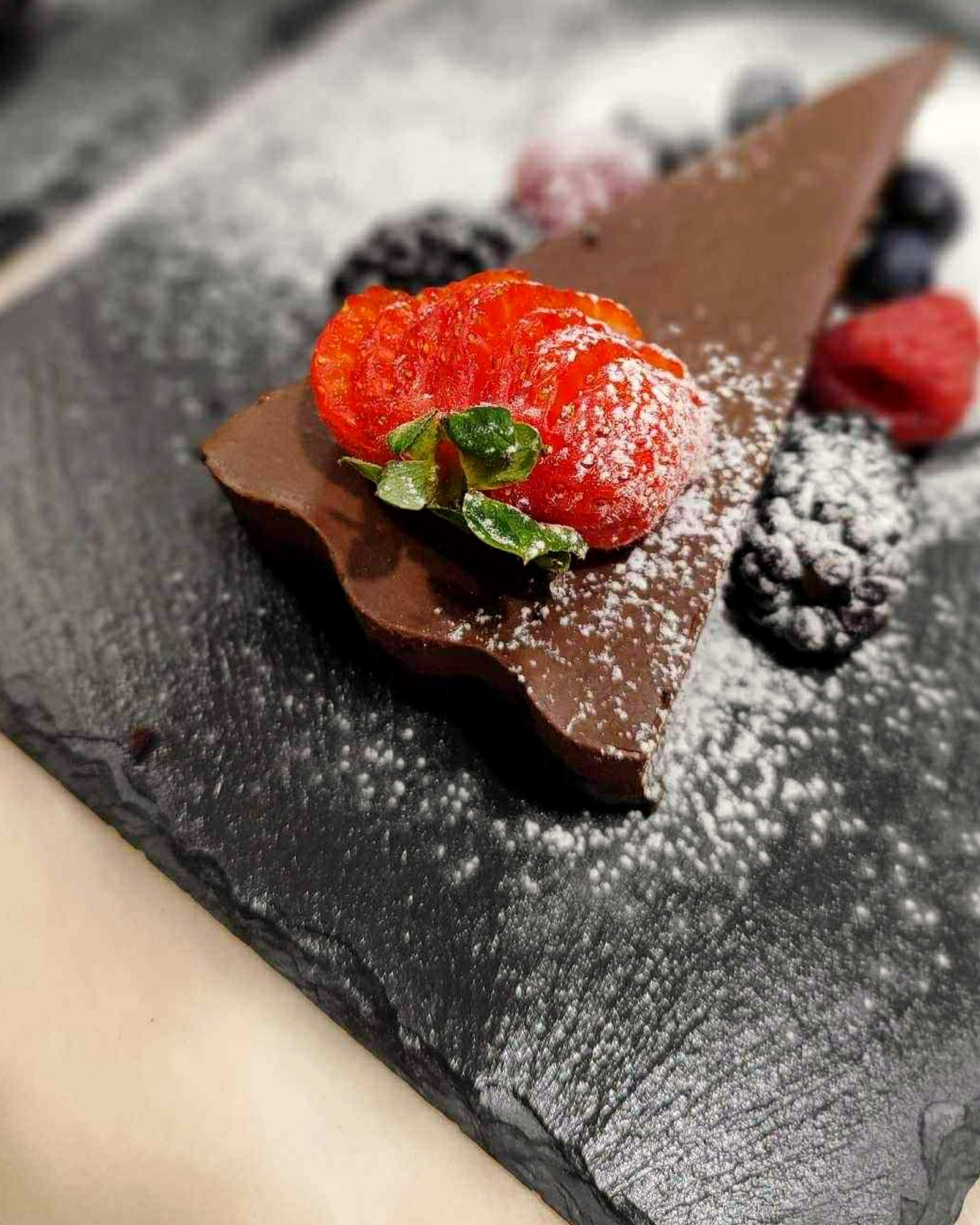 Chocolate torte with macerated strawberries and berries, dusted with icing sugar and served on slate
