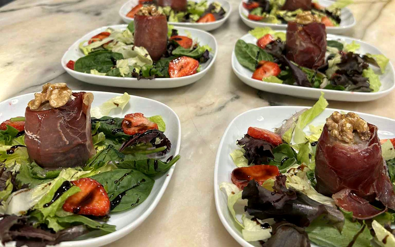 Two rows of identical plated starters ready to leave the pass at a villa dinner
