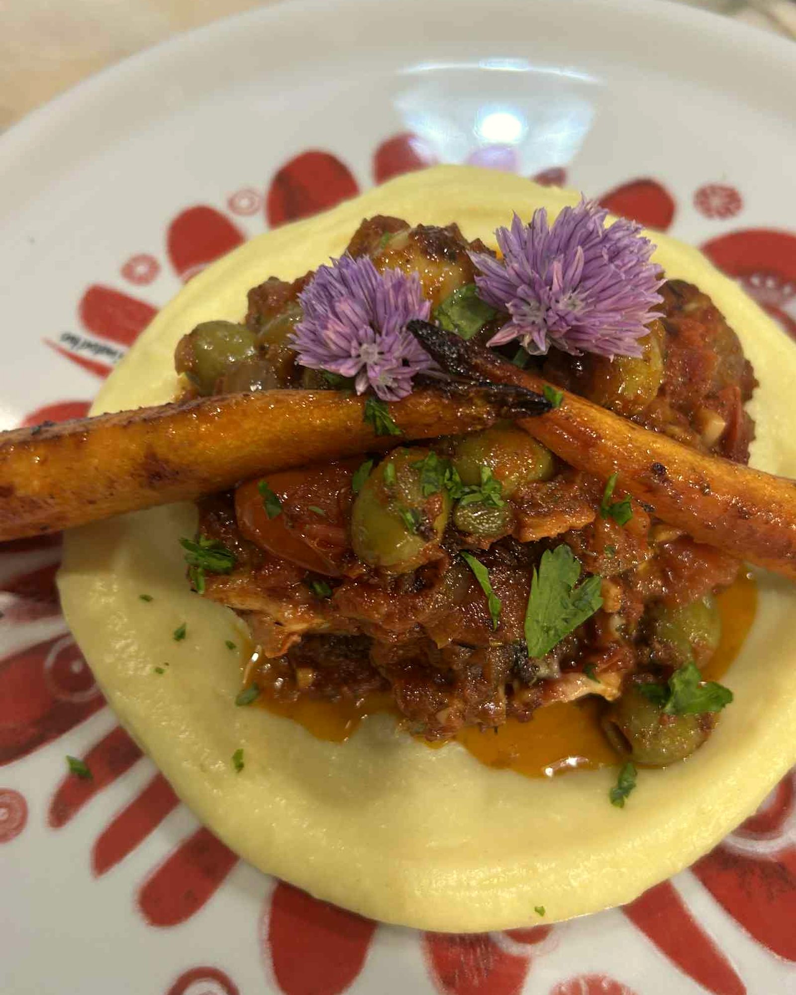 Slow-cooked pork with green olives, roast carrot and chive flowers on smooth potato purée