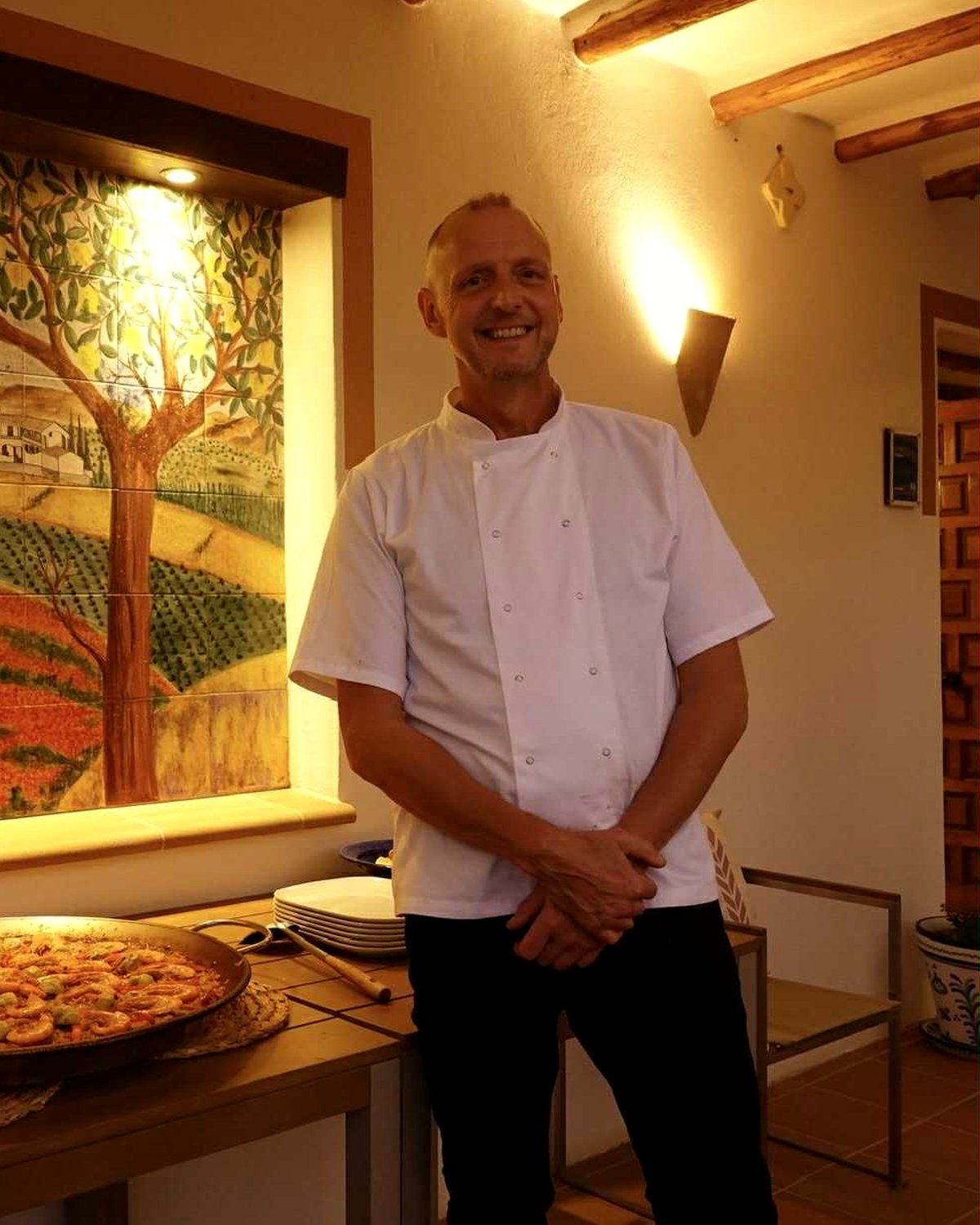 Simon, private chef, smiling beside a fresh paella
